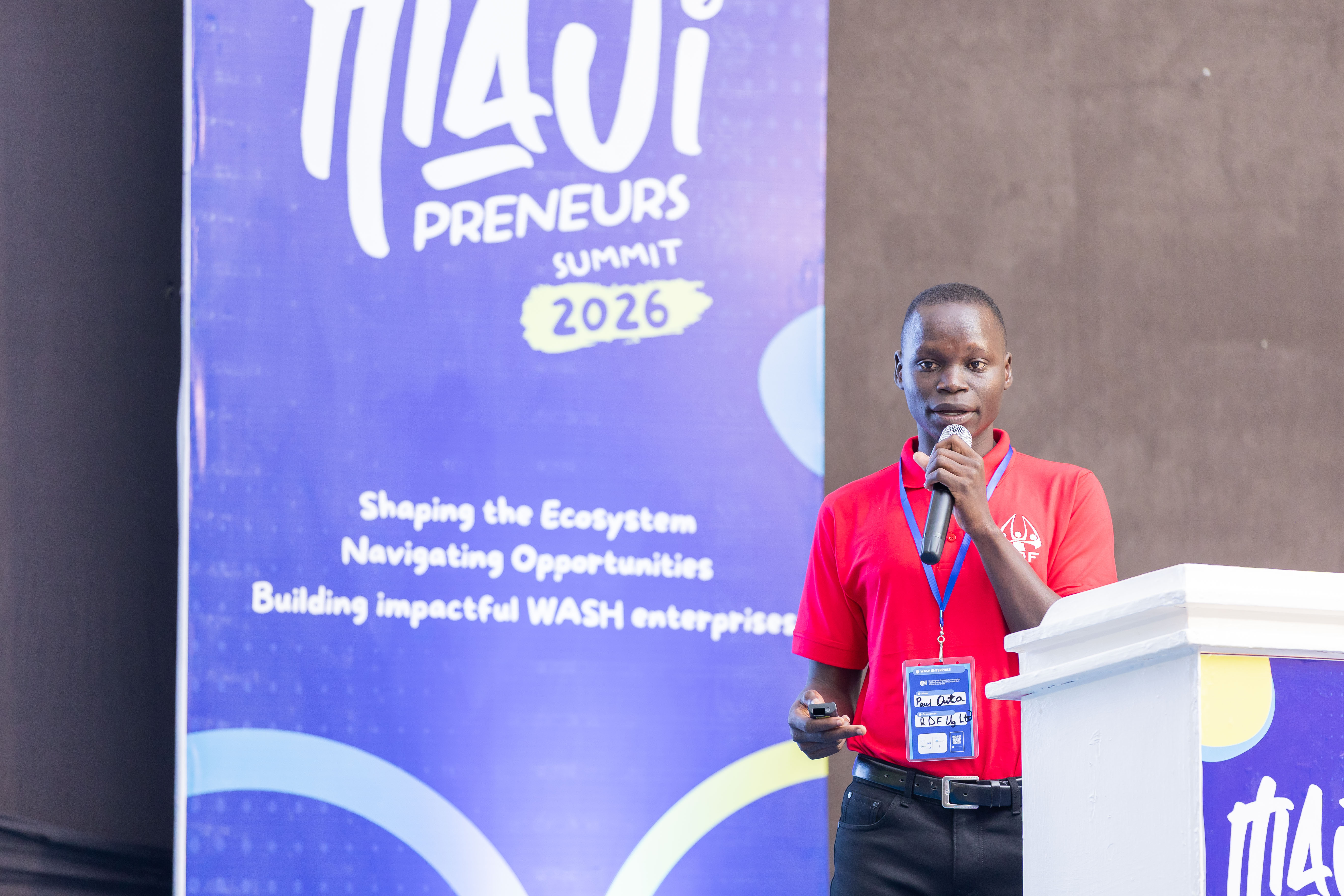 RDF Resource Mobilisation Officer Paul Outa speaking at the Majipreneurs Summit 2026 plenary, with the WASH enterprises theme banner behind him